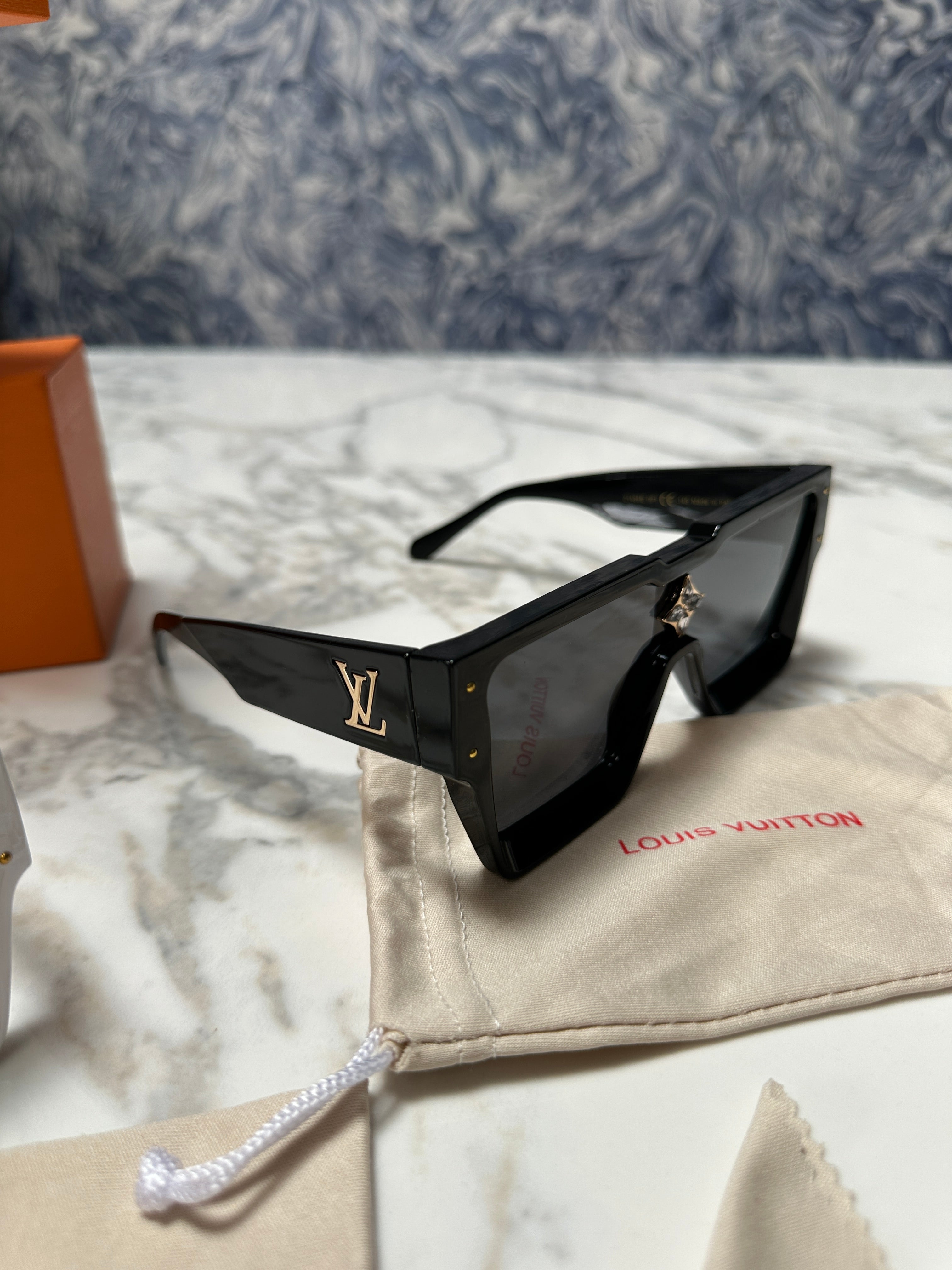 Black sunglasses with a brand logo on a textured surface
# Louis Vuitton Cyclone Sunglasses – Black Acetate Designer Sunglasses

Make a bold statement with the **Louis Vuitton Cyclone Sunglasses**, an iconic luxury eyewear style featuring an oversized, angular silhouette and distinctive LV detailing. Crafted with a bold black acetate frame, black lenses and refined gold-colour hardware, these designer sunglasses combine contemporary fashion with unmistakable Louis Vuitton style.

The Cyclone sunglasses feat